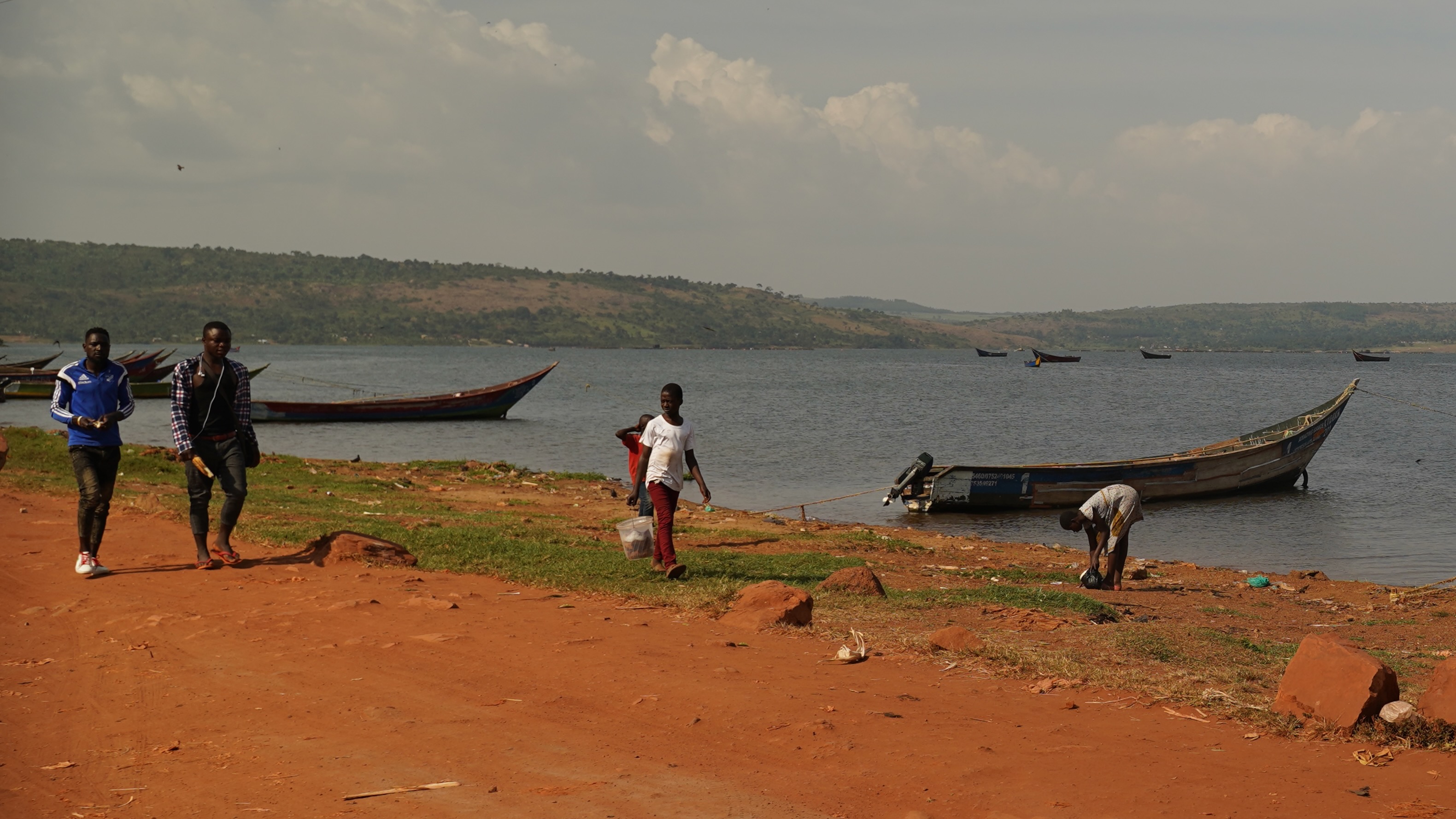 Lake Victoria, people walk by as a young girl picks up small fish left by the fishermen